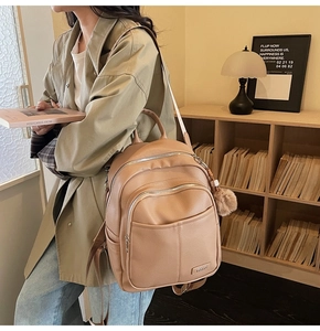 Detail view of khaki pebbled leather backpack with side pockets and plush charm accessory