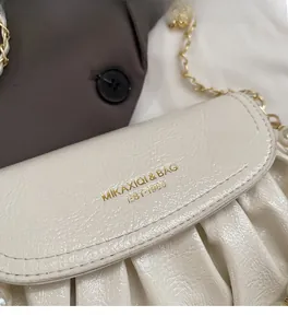 Detail of white pleated faux leather shoulder bag with gold logo and metal chain strap