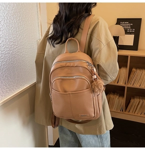 Detail of light brown lychee grain leather backpack with plush ball charm and logo
