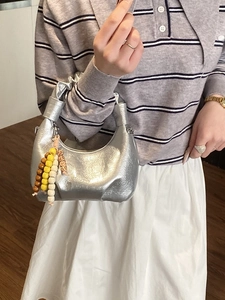 Metallic silver hobo handbag with ruched handle and colorful beaded charm on a model
