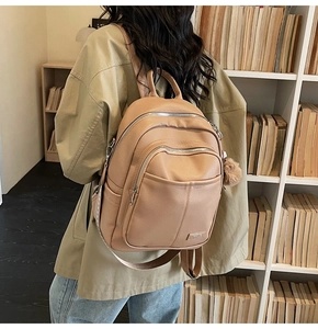 Close-up of light brown textured leather backpack with zipper pockets and plush ball charm