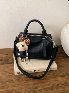 Large vintage black faux leather Boston bag with plush dog charm on wooden table
