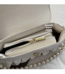 Detail of smooth gold zipper and pearl strap on ivory pleated cloud bag