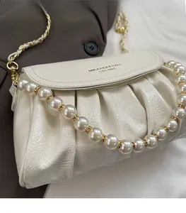 Detail of white pleated handbag featuring pearl bead handle and gold metal chain strap