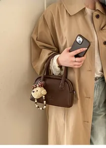 Detail of dark brown pebble leather handbag with plush dog charm and beaded wrist strap