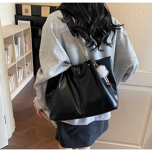 Detailed view of black faux leather tote with gold chain strap and plush ball charm