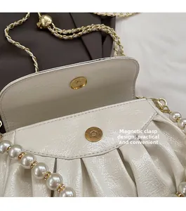 Detail of the cream pleated bag showing the magnetic buckle and pearl chain strap