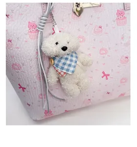 Close-up of white plush bear pendant with blue checkered scarf on a pink handbag