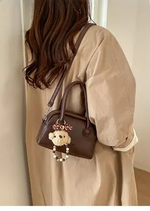 Detail of dark brown lychee leather bowling bag with twin handles and bear charm