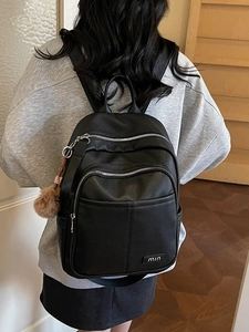 Stylish black leather backpack for women with silver zippers and a cute plush pom pom charm