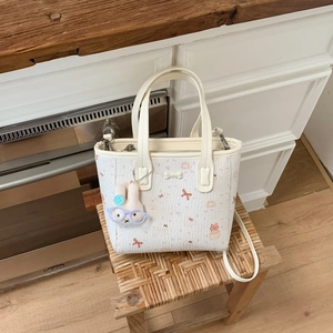 Détail d'un sac à main blanc à imprimé cartoon avec texture litchi et breloque lapin