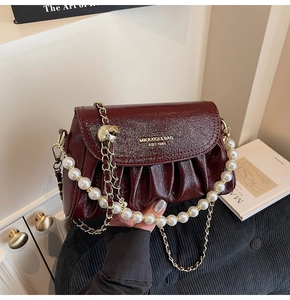 Detail of burgundy glossy pleated handbag with large pearl handle and metal chain