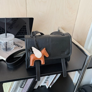 Detail of black leather flap crossbody bag featuring a decorative orange pegasus charm
