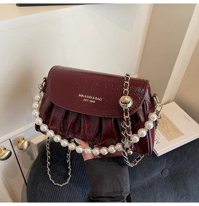 Detail of burgundy glossy pleated shoulder bag with pearl handle and gold chain strap