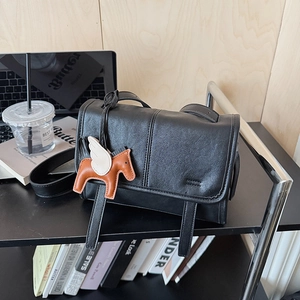 Close-up of black matte leather shoulder bag with a brown pony charm on a desk