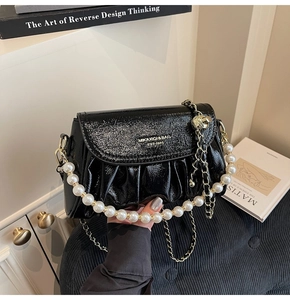 Detailed macro view of black pleated patent leather bag with white pearl handle chain