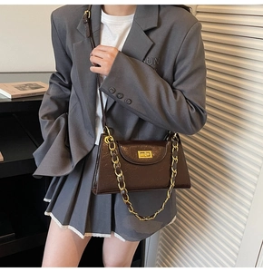 Détail d'un sac en cuir verni marron foncé avec fermoir doré et bandoulière en chaîne