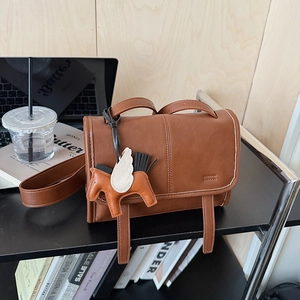Brown leather crossbody bag with a horse charm next to a laptop and magazines