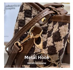 Detail of high-gloss gold hardware hook and houndstooth texture on vintage bucket bag