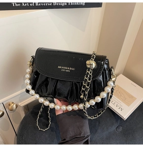 Close-up of black glossy cloud bag with decorative large pearl chain and gold hardware