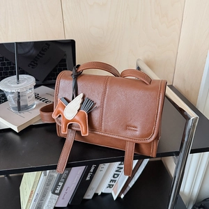 Detail of a dark brown leather flap bag with a horse-shaped charm on a desk