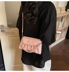 Detail of pink pleated cloud bag with pearl strap and gold chain shown on shoulder