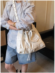 Close-up of ivory bucket bag with punk rivets, motorcycle buckles and tassel details
