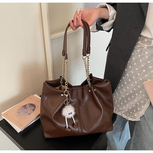 Detail of dark brown leather tote bag with thick gold chain strap and plush monster charm