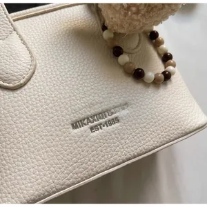 Detail of cream pebbled leather bucket bag with silver logo and beaded plush charm