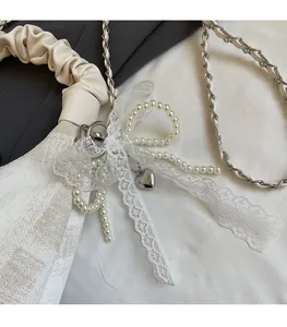 Close-up of pearl bow charm with lace ribbons and heart pendant on a pleated bag