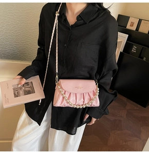 Detail of pink pleated crossbody bag with pearl handle and golden brand logo engraving