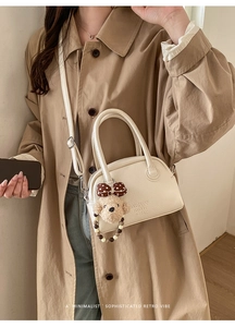 Close-up of white pebble leather bowling bag with cute plush bear charm and crossbody strap
