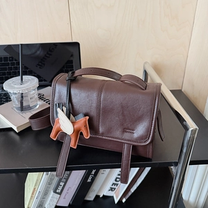 Detail of dark brown leather crossbody bag with decorative horse charm in a workspace setting