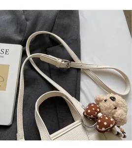 Detail of white pebble grain leather bag with silver buckle and plush bear charm