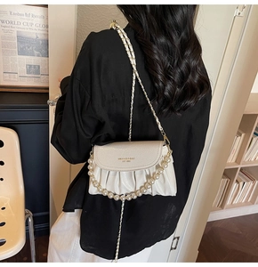 Detail of white pleated shoulder bag with elegant pearl and metal chain straps