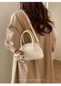 Detail van crème-witte lederen mini-tas met teddybeer-bedel op een trenchcoat