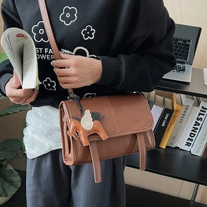 Brown retro leather messenger bag with decorative straps and a horse charm on a desk