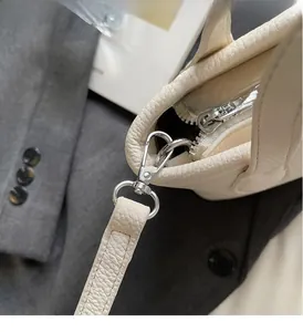 Detail of silver metal hook fastener and lychee grain leather strap on off-white bucket bag