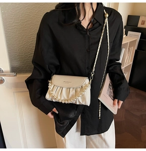 Close-up of beige pleated handbag with gold chain strap and pearl bead decoration