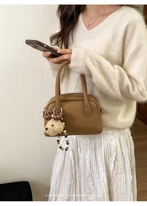 Close-up of khaki Boston bag featuring embossed letters and a cute plush bear charm