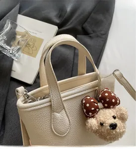 Detail of off-white lychee grain leather handbag with cute teddy bear charm and silver hardware