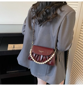 Macro view of burgundy pleated glossy leather bag featuring elegant pearl handle and chain