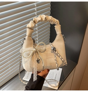 Detail of beige dumpling bag featuring lace bow, pearl charms and metal chain strap