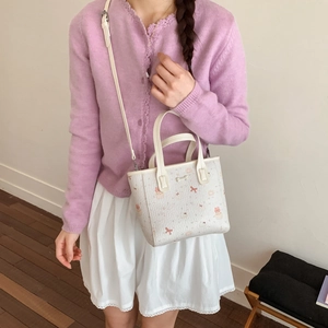 Gros plan d'un sac blanc à motifs nœuds roses porté avec un pull lavande et une jupe