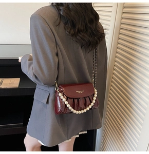 Detail of burgundy ruched patent leather bag with white pearls and gold chain strap