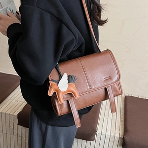 Detail of vintage brown leather crossbody bag with a horse charm in a warm room