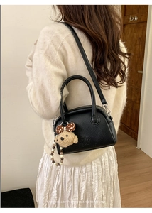 Detail of black lychee grain bowling bag with plush bear charm and crossbody strap