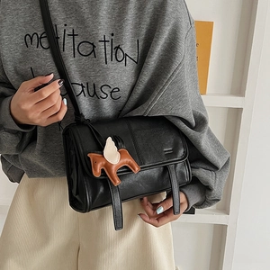 Close-up of a black vintage crossbody bag with a horse charm on a neutral background
