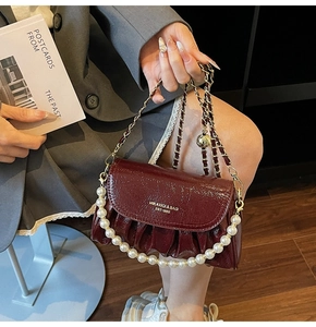 Detail of burgundy ruched patent leather bag with pearl handle and gold chain strap
