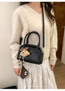 Detail of black textured leather baguette bag with plush bear charm and crossbody strap